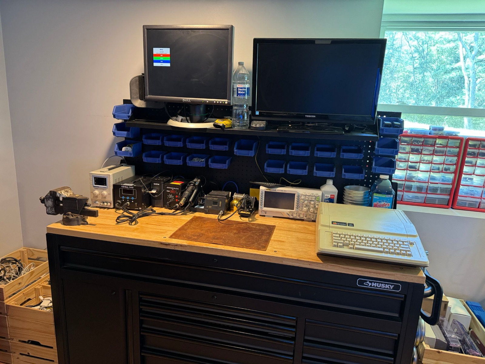 Electronics workbench with bench vise, programmable power supply, soldering and hot-air rework stations, oscilloscope, and an Apple IIe under repair